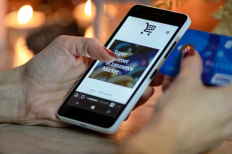 Woman using smartphone for online shopping with credit card in hand, festive background lighting