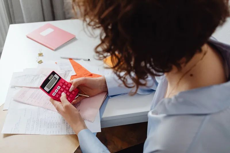 Person calculating a monthly budget with a calculator and notebook at a desk