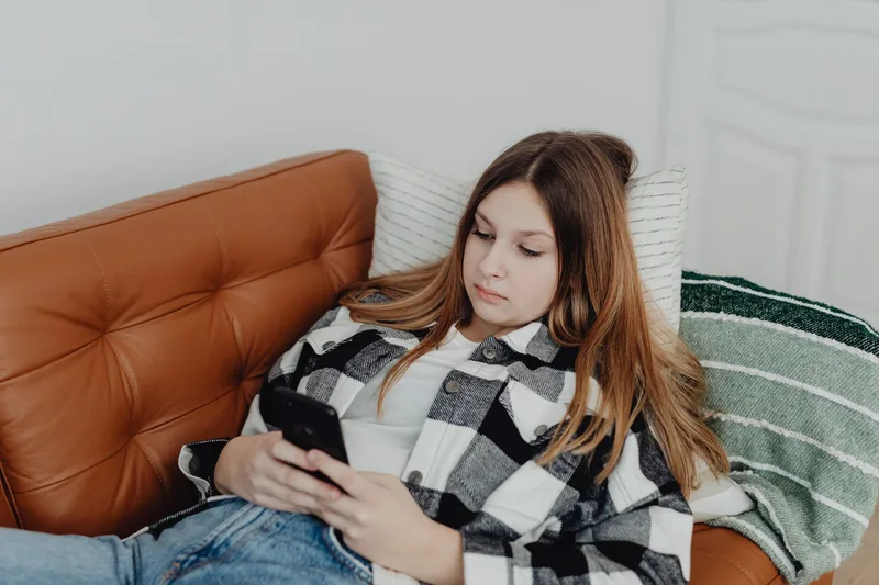 Person relaxing at home while browsing a smartphone, illustrating the kind of interruption that pulls a shopper away mid-checkout