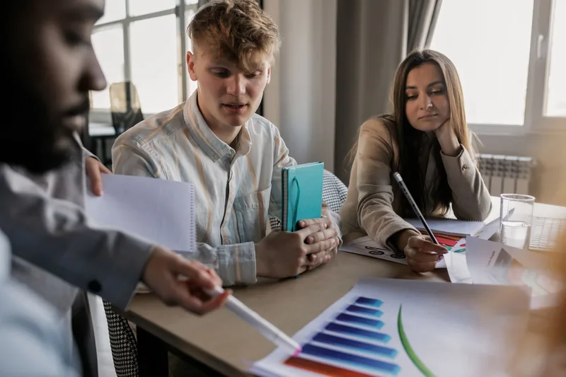 Team reviewing performance data and a timeline on a table during a marketing meeting