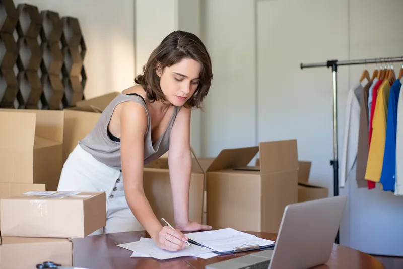 Ecommerce seller reviewing her online store from a home office desk with packaging boxes nearby